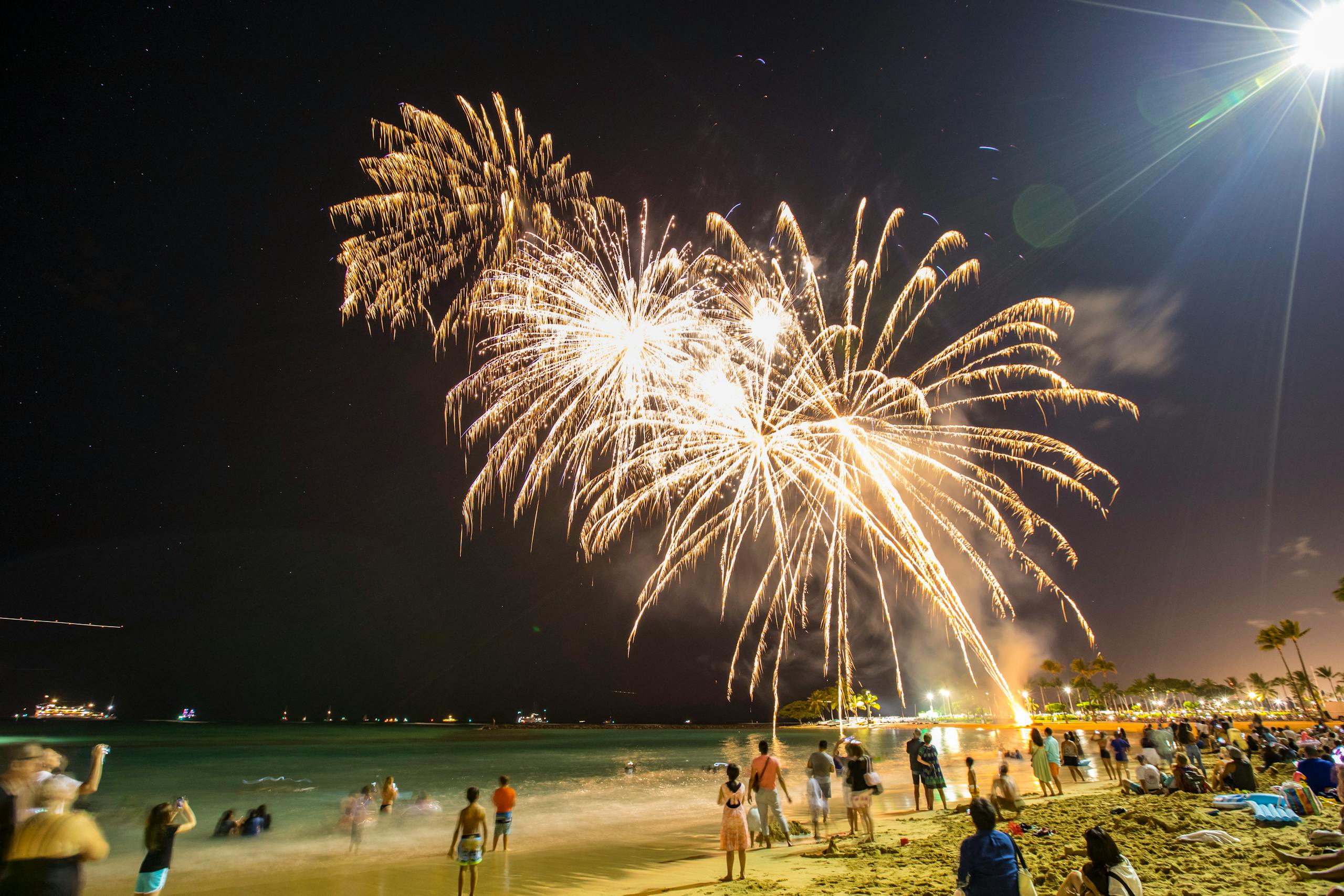 Colorful fireworks light up the night sky over a crowded beach, creating a festive atmosphere.